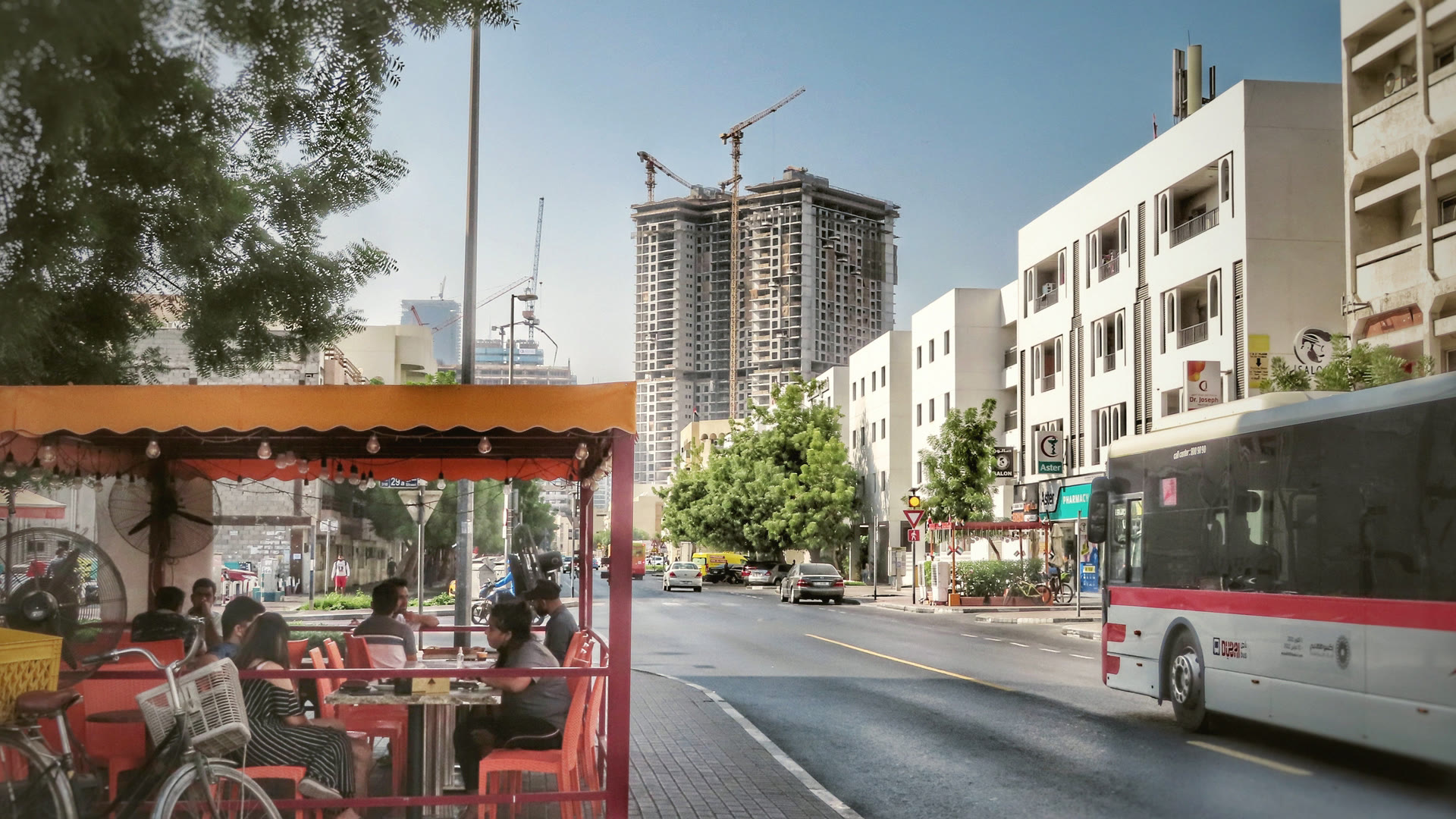 An ordinary Dubai street on a weekday morning: a café terrace, a bus and low-rise apartment buildings