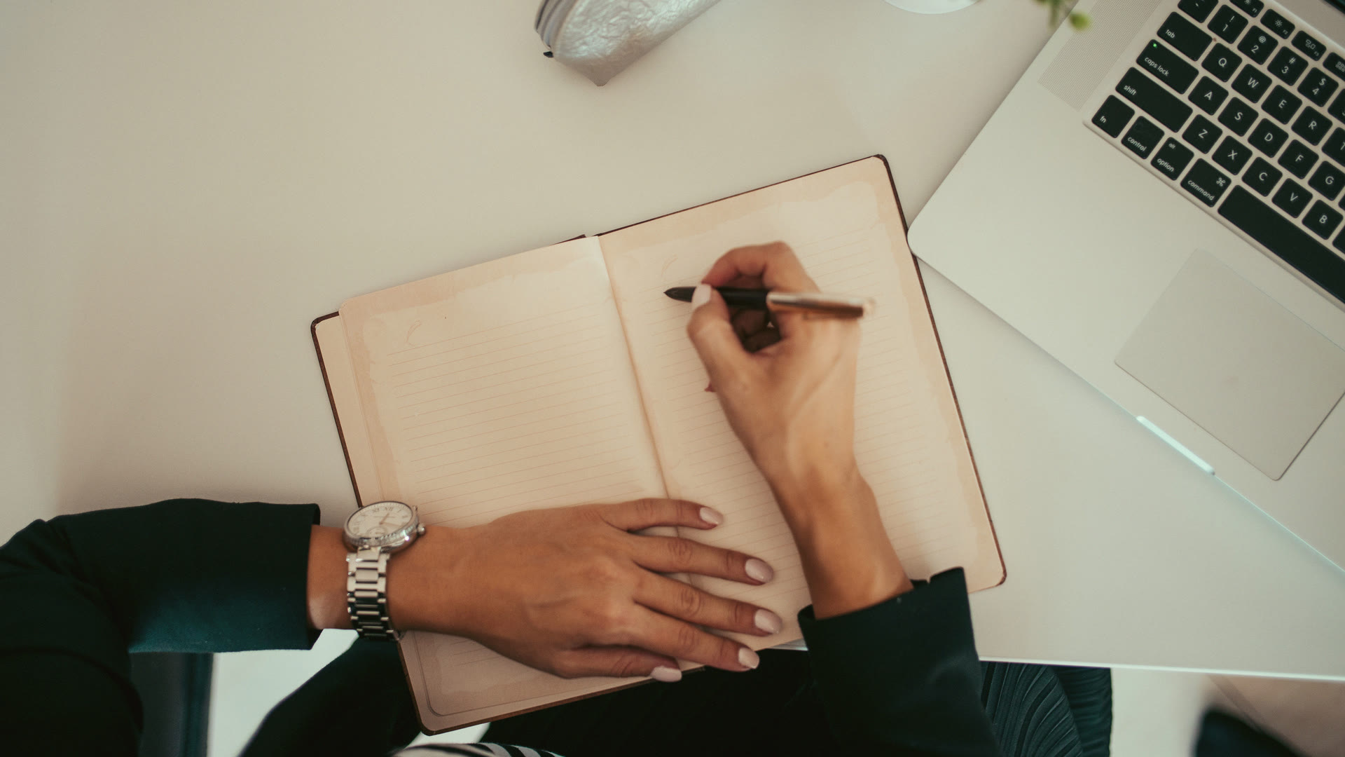 Filling in a notebook beside a laptop while preparing a registration